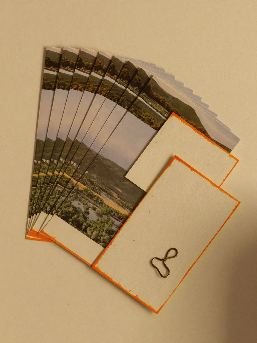 Fanned stack of landscape photo prints with blank orange-edged cards and a small brass clip on warm cream paper