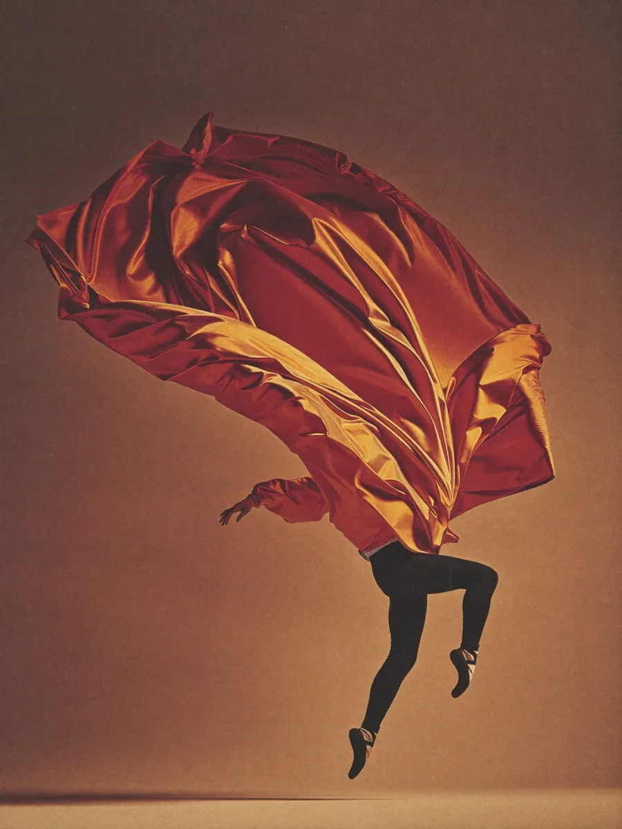 AI-generated fine-art photograph of a ballet dancer mid-leap with a ribbon of signal-orange silk arcing through the air behind her